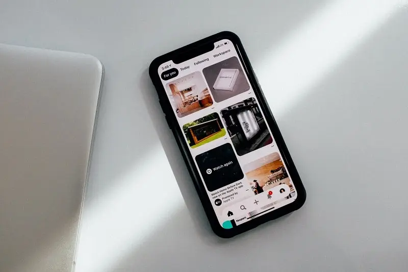 Foto de um celular preto sobre uma mesa branca. Na tela tem um feed do Pinterest para representar o Pinterest Ads.