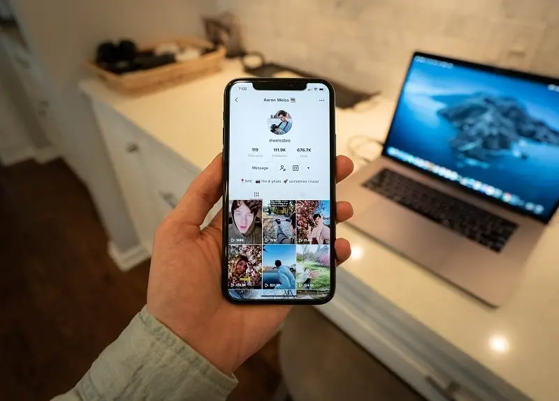 Foto de uma mão segurando um celular. Na tela está aparecendo alguns vídeos do TikTok Ads e outros orgânicos.