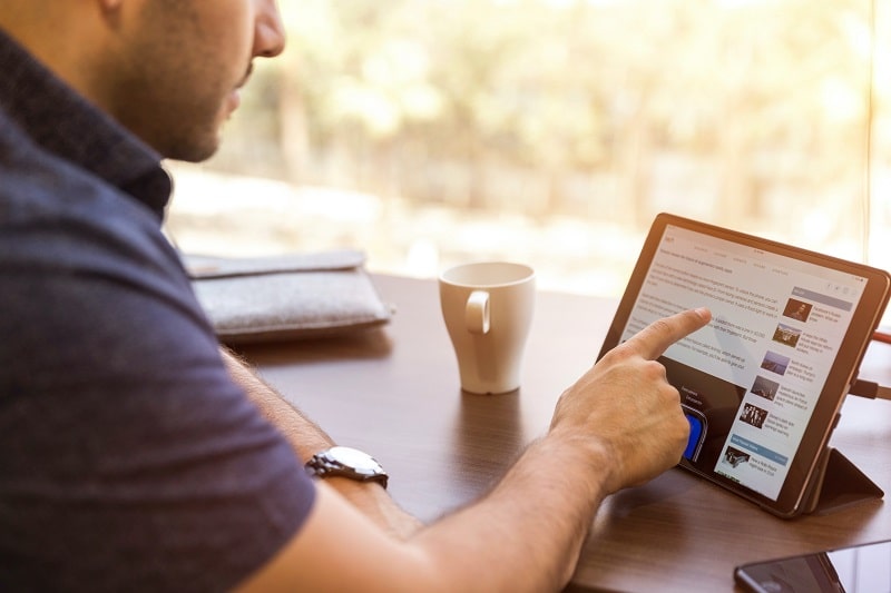 foto de um homem sentando numa mesa com um braço apoiado sobre ela apontando para a tela de um tablet que mostra um a anuncio feito no LinkedIn Ads