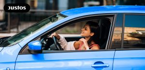 Mulher dirigindo carro azul com um símbolo da Justos no canto esquerdo