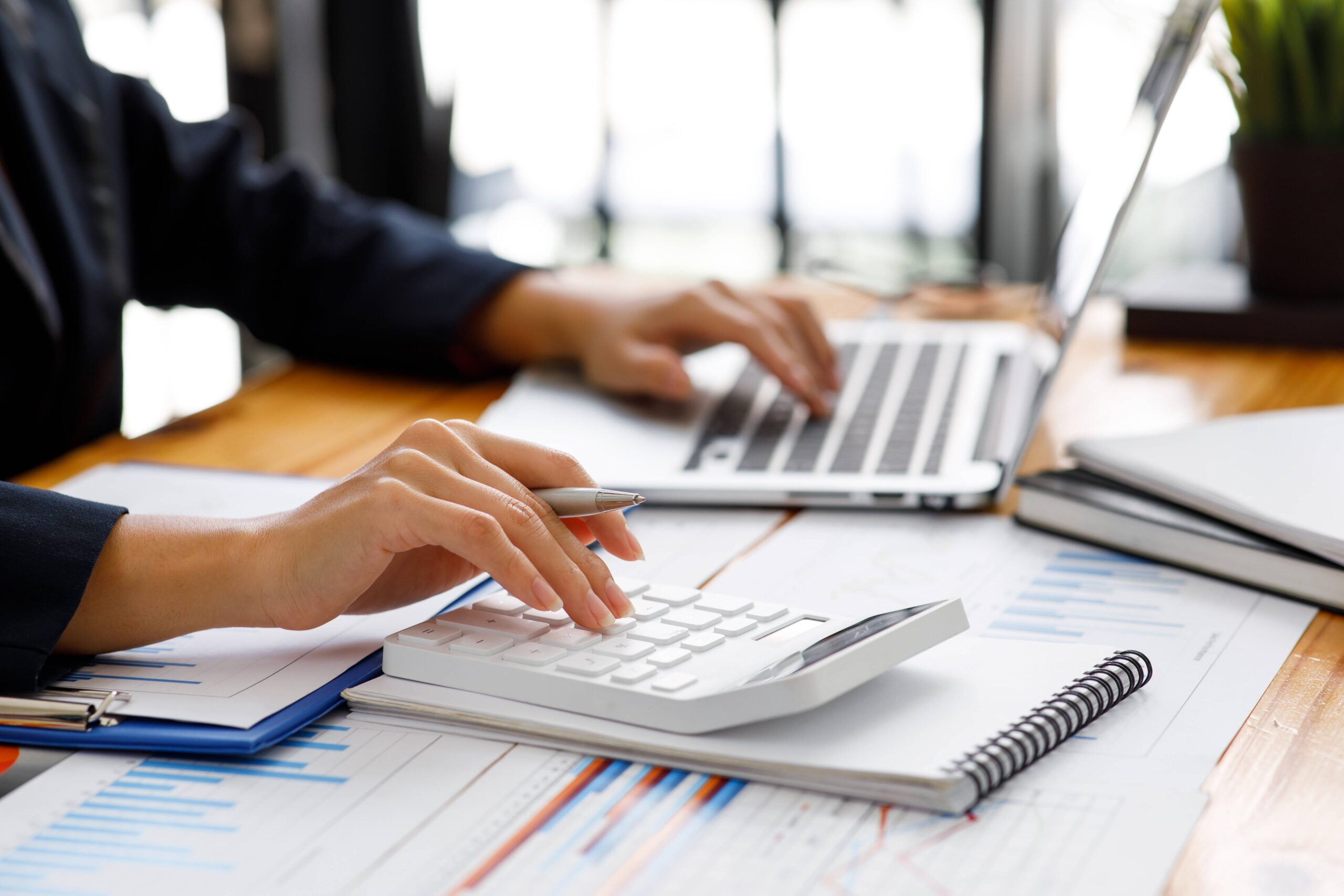 Na imagem, uma mulher de negócios usa a calculadora para fazer contas enquanto digita os resultados no notebook. Contabilidade fiscal, gestão financeira, conta simples.